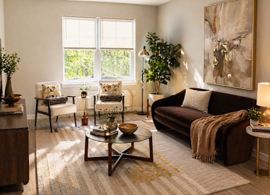 A living room at the Rail North Bergen with a brown couch, a coffee table, and a large painting on the wall.