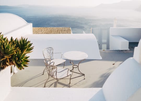 A table and chairs are on a patio overlooking a mountainous landscape.