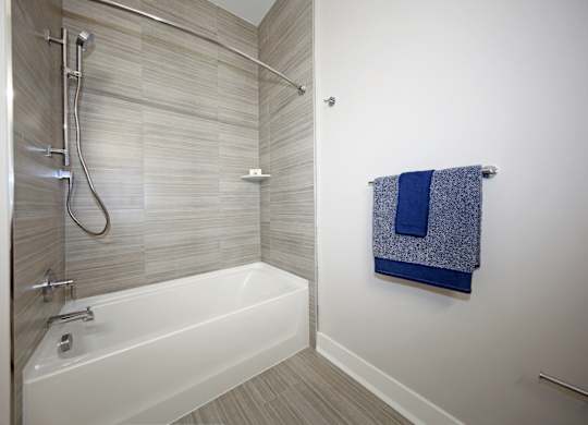 A white bathtub with a shower head and a towel hanging on the wall.