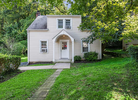 A small house with a white door and windows surrounded by greenery.
