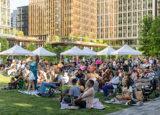 A large group of people are sitting on the grass in a park.
