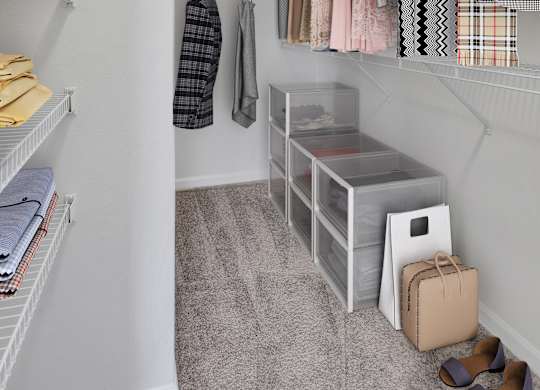 A small closet with clothes hanging and shoes on the floor.