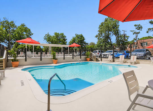 A large outdoor swimming pool with red umbrellas and lounge chairs.