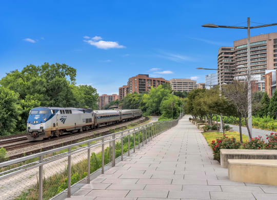 a train on the tracks near a sidewalk with trees and buildings