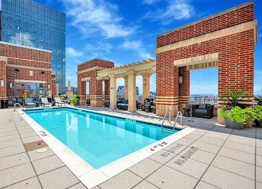 A pool surrounded by a brick wall with a clear blue sky in the background.