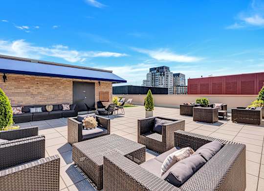 A patio with black wicker furniture and a red building in the background.