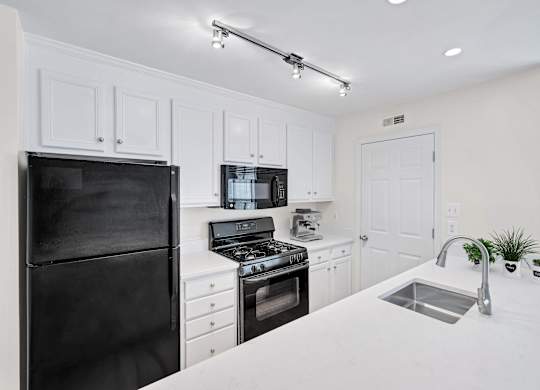 A black refrigerator is on the left in a white kitchen.