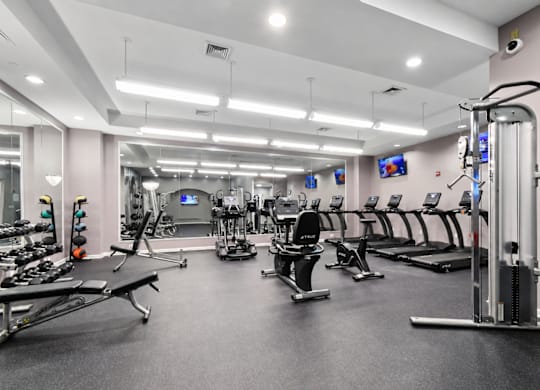 A spacious gym with various exercise equipment and mirrors on the wall.