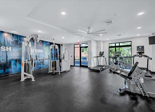 A gym with a variety of equipment including treadmills, weights, and a fan.