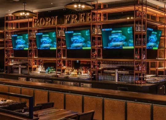 a bar with tvs on the wall and wooden tables and chairs