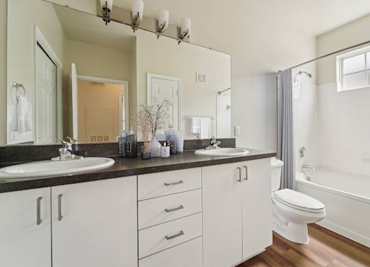 A white bathroom with a double sink and a toilet.