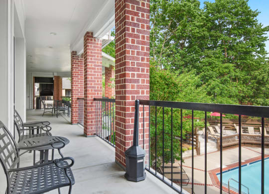 a balcony with two chairs and a table and a pool in the background