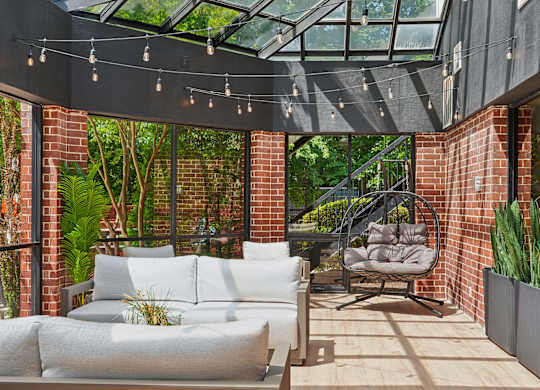 A patio with a white couch and a chair under a glass roof.
