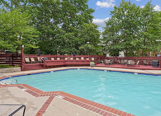 A large outdoor swimming pool surrounded by trees and a red fence.