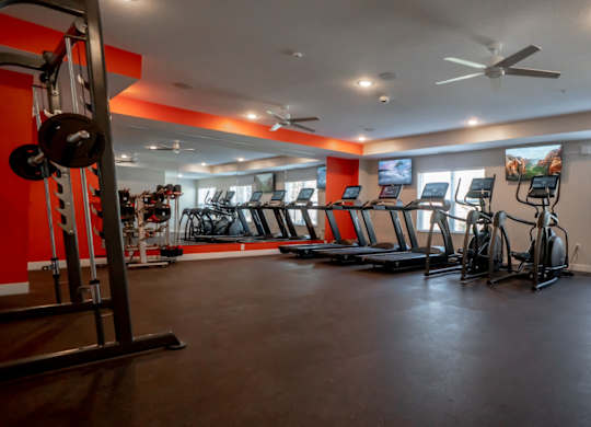 A gym with a variety of exercise equipment including treadmills, stationary bikes, and weight machines.