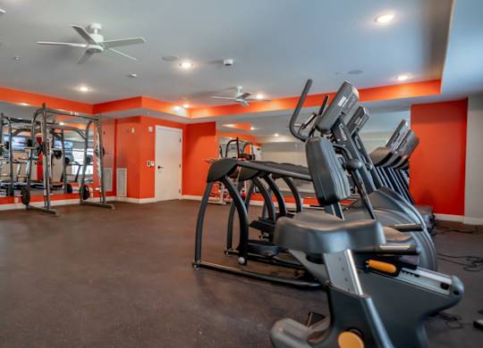 A gym with orange walls and a variety of exercise equipment.