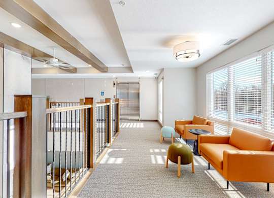 A long hallway with orange chairs and tables on the right side.