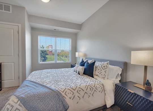 A bedroom with a large bed and a window with blinds.