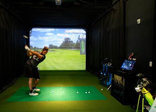 A man is playing golf indoors on a green mat.