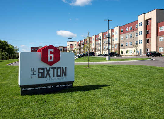 A sign for The Sixton Apartments is in front of a building.