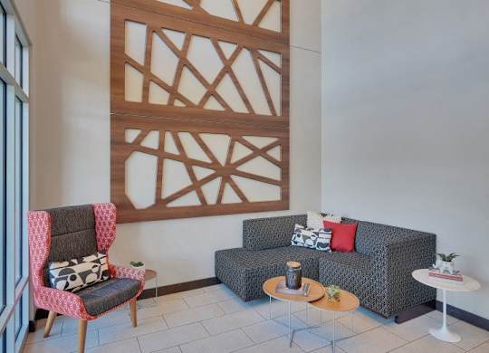 A living room with a grey couch, a red chair and a wooden wall panel.