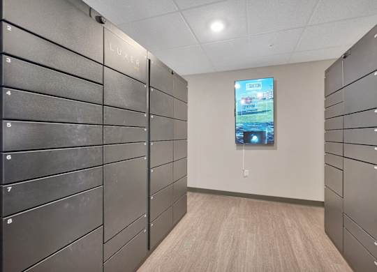 A hallway with a row of lockers on the left and a TV screen on the right.
