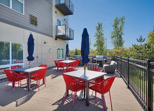 A patio with red chairs and tables is surrounded by a black fence.