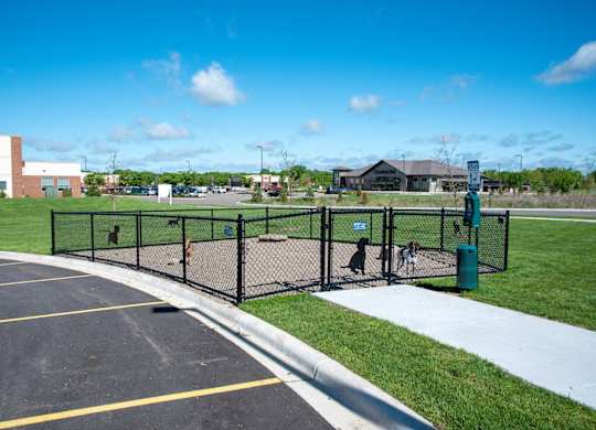 A parking lot with a black fence and a green trash can.