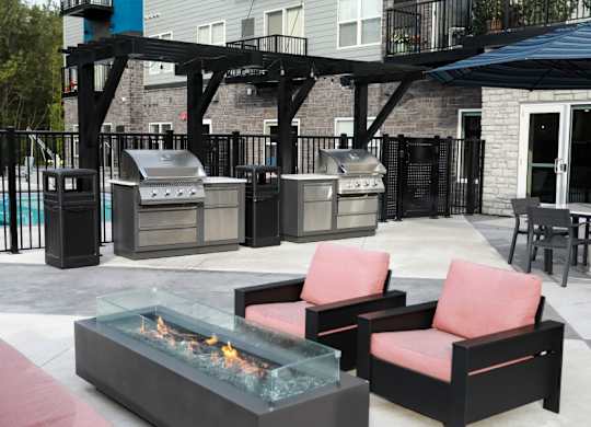 A patio with a fire pit, chairs, and a grill.