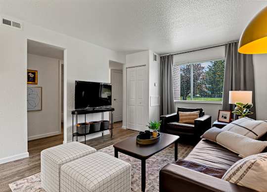 A living room with a brown couch, a white chair, and a television. at Vivo Toledo Apartments, Ohio, 43607