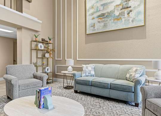 A living room with a grey couch, a grey armchair, a white coffee table, and a large abstract painting on the wall.
