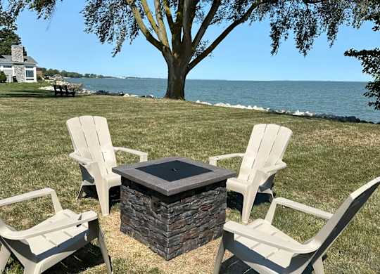 A fire pit surrounded by three chairs on a lawn.