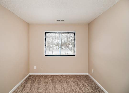 A bedroom with a window and carpeted floor.