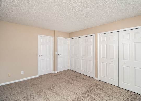 A room with three white doors and beige walls.