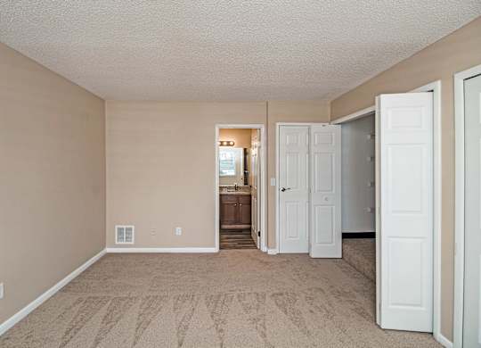 A room with beige walls and carpeting, with a doorway leading to another room.