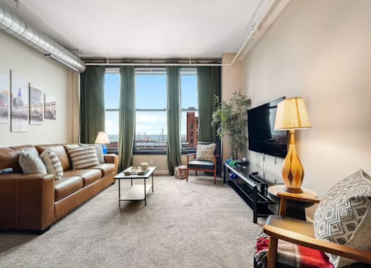 A living room with a brown leather couch, a coffee table, a flat screen TV, and a large window with a view of the city.