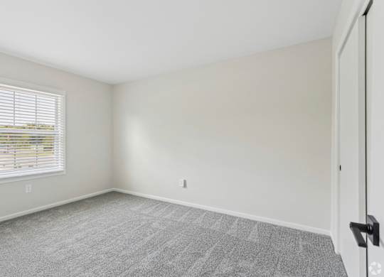 A room with a carpeted floor and a window with blinds.