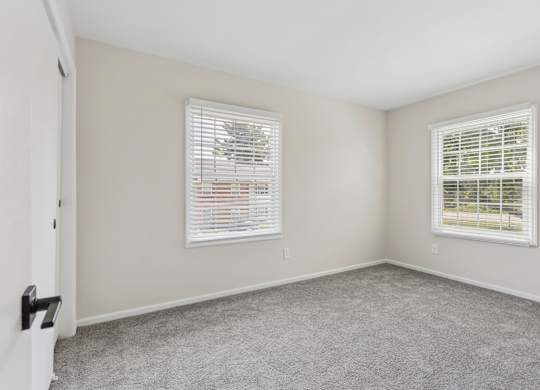 A room with two windows and carpeted floor.