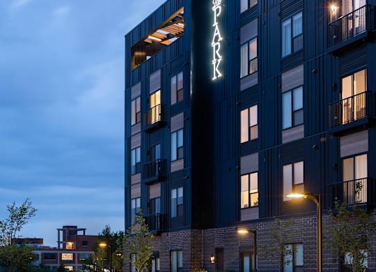 A modern apartment building named "SPARK" is lit up at dusk.