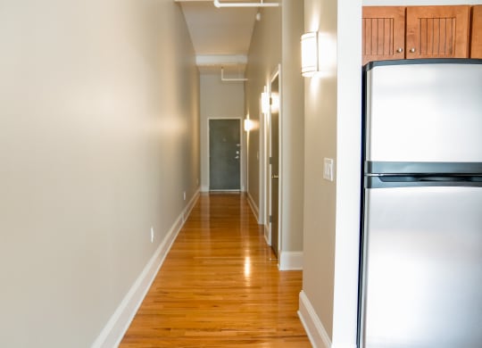 a hallway with white walls and wood floors and a stainless steel refrigerator