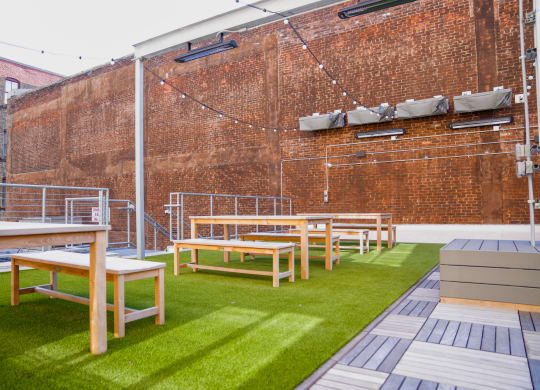 a row of tables and benches on a lawn in front of a brick wall at East 4th Street, Cleveland, 44115