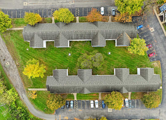 An aerial view of a grey building surrounded by a parking lot and trees.