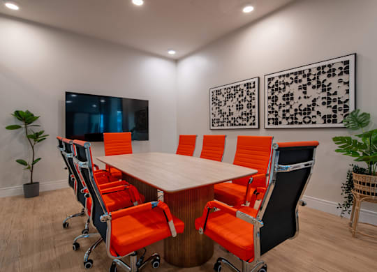A conference room with a long table and orange chairs.