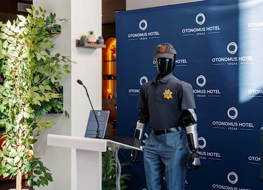 A mannequin dressed in a police uniform stands in front of a backdrop for Otonomus Hotel.