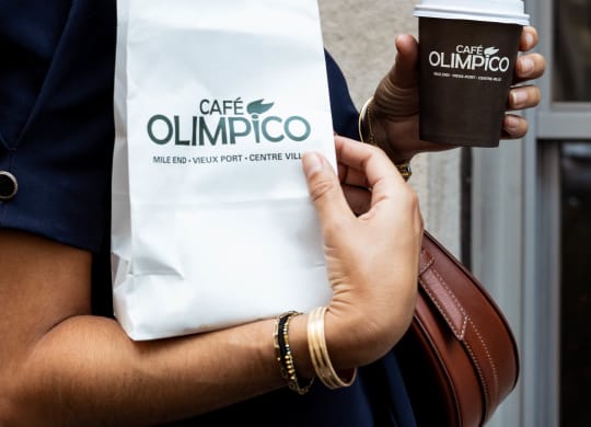 a woman holding a cup of coffee and a bag of cafe olimpicco