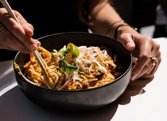 a woman eating a bowl of noodles with chopsticks