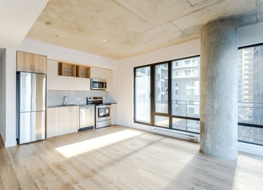 an empty living room with a kitchen and a large window