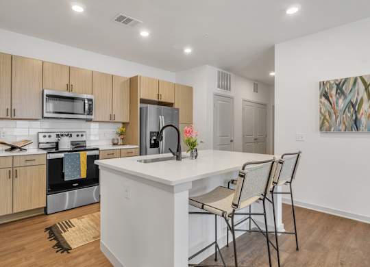 a kitchen with a large island with a white counter top and three chairs