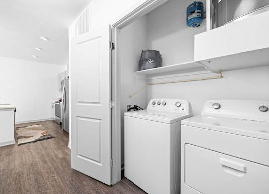 a white laundry room with washer and dryer and a door to a kitchen