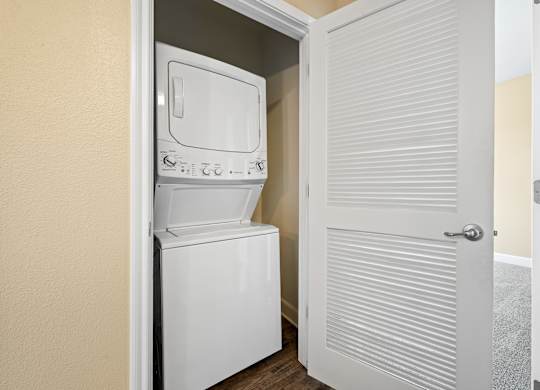 A white stackable washer and dryer is installed in a narrow space between two walls.